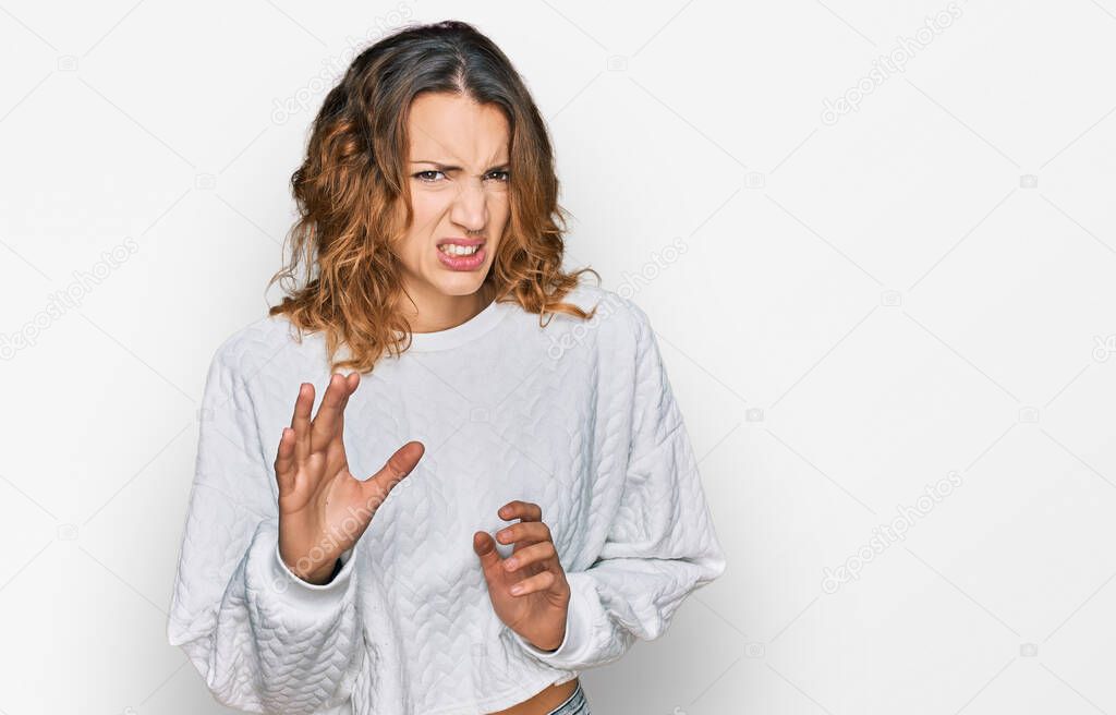 Beautiful young caucasian woman wearing casual winter sweater disgusted expression, displeased and fearful doing disgust face because aversion reaction. with hands raised 