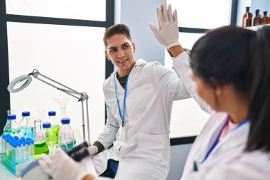 Erkek ve kadın bilim adamları laboratuarda elleri havada beşlik çakıyor.