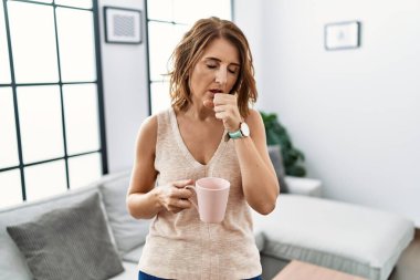Orta yaşlı bir kadın evde kahve içerken kendini iyi hissetmiyor ve soğuk algınlığı veya bronşitin belirtisi olarak öksürüyor. sağlık hizmeti kavramı. 