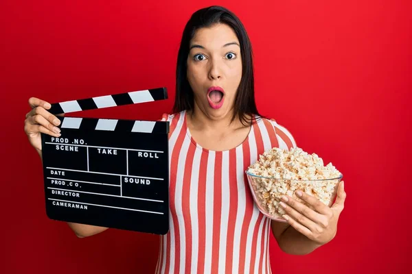 Młoda Latynoska Kobieta Trzymająca Film Wideo Klapką Popcornem Przerażona Zszokowana — Zdjęcie stockowe
