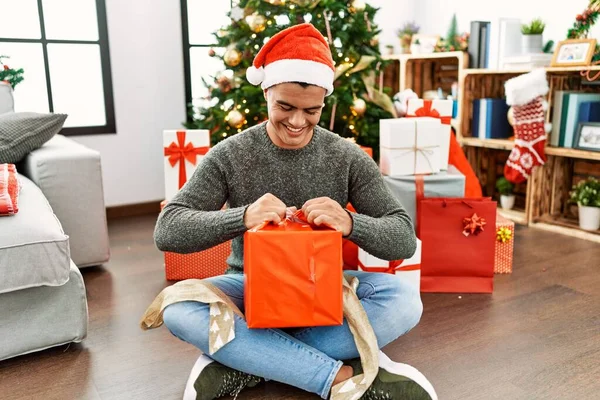 Jovem Hispânico Desempacotando Presente Sentado Árvore Natal Casa — Fotografia de Stock