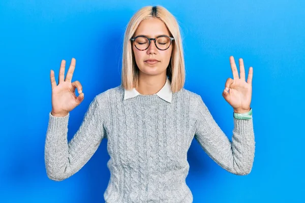 Beautiful blonde woman wearing glasses relax and smiling with eyes closed doing meditation gesture with fingers. yoga concept.