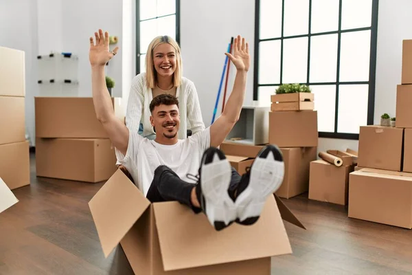 Young caucasian couple smiling happy playing with cardboard box as a car at new home.