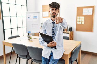 Ofiste masasında oturan sakallı İspanyol bir adam kamerayı işaret ediyor ve kendine güveni tam bir jest yapıyor. 