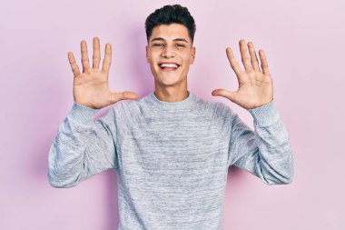 Gündelik kıyafetler giyen genç İspanyol adam on numarayı gösterip işaret ederken kendinden emin ve mutlu bir şekilde gülümsüyor.. 