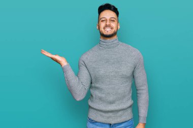 Gündelik giysiler giyen genç Arap adam neşeli bir şekilde gülümsüyor ve avuç içi kameraya bakıyor.. 