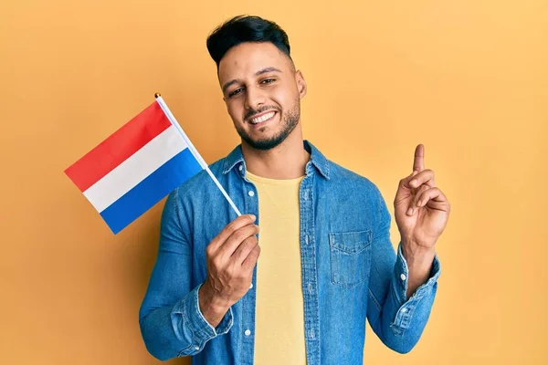 Ung Arabisk Man Håller Holland Flaggan Ler Glad Pekar Med — Stockfoto