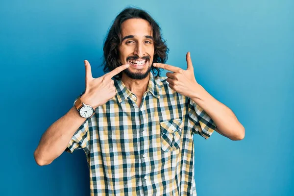 若いヒスパニック系の男は陽気な笑みを浮かべてカジュアルな服を着て指の歯と口を指しています 歯の健康の概念 — ストック写真