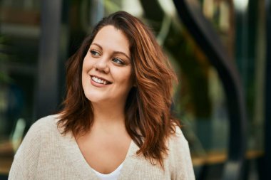 Genç İrlandalı artı cüsseli kız gülümseyerek şehirde mutlu mesut duruyor..