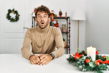 Masada sakallı genç yakışıklı adam yılbaşı süslemesi yüzünden korkmuş ve şok olmuş bir şekilde oturuyor.. 
