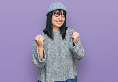 Şirin yün şapka takan genç İspanyol kadın çok mutlu ve heyecanlı. Kolları havada, gülümseyen ve başarı için çığlık atan kazanan bir jest yapıyor. kutlama konsepti. 