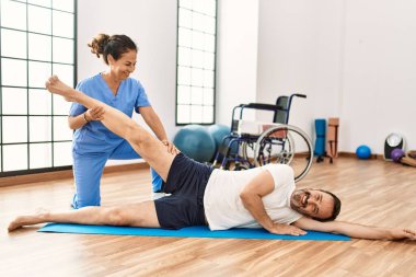 Orta yaşlı bir adam ve kadın fizyoterapi kliniğinde rehabilitasyon seansı yaparken gülümsüyor.