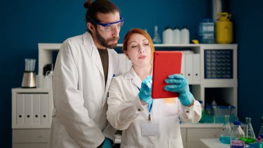 Laboratuvarda dokunmatik ped kullanan bilim adamı ve kadın üniforması giyiyor.