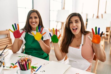 İki Latin öğrenci mutlu bir şekilde gülümsüyor. Sanat okulunda boyalı eller gösteriyorlar..