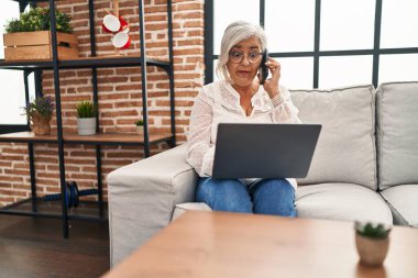 Evde bilgisayarla konuşan orta yaşlı bir kadın.