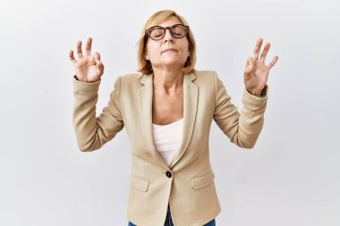 Orta yaşlı sarışın iş kadını izole edilmiş arka planda duruyor rahatlamış ve parmaklarıyla meditasyon hareketi yaparken gözleri kapalı gülümsüyor. yoga konsepti. 