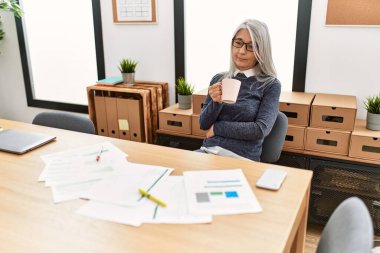 Ofiste çalışırken gülümseyen beyaz saçlı iş kadını.