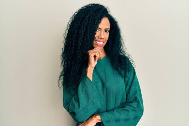 Orta yaşlı Afro-Amerikalı kadın, günlük kıyafetler giyip kameraya kollarını kavuşturup, çenesini kapatarak gülümsüyor. Olumlu düşünmek. 