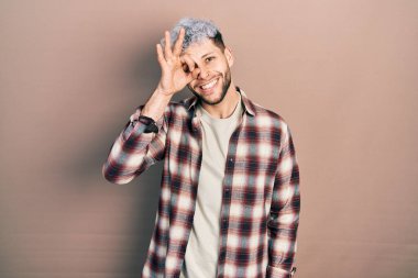 Modern boyalı saçlı, rahat gömlekli, mutlu gülümseyen genç İspanyol adam. Elleri gözlerinde, parmaklarının arasından bakıyor. 