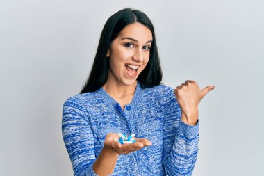 Genç İspanyol kadın elinde haplarla başparmağını kaldırıyor ve ağzı açık gülümsüyor. 