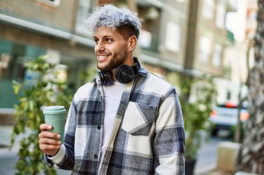 Genç İspanyol adam şehirde kahve içerken kulaklık takıyor..
