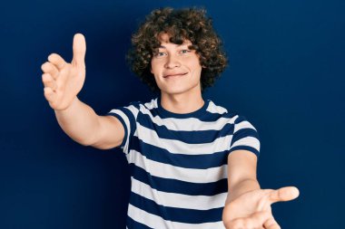 Sıradan çizgili tişört giyen yakışıklı genç adam sarılmak için kollarını açmış kameraya bakıyor. Mutluluğu kucaklayan neşeli bir ifade.. 