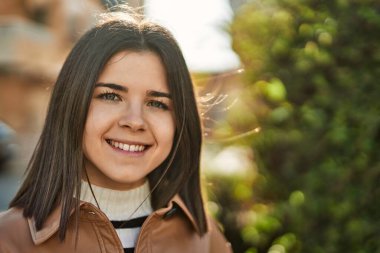 Genç, güzel, esmer kadın dışarıda mutlu bir şekilde gülümsüyor.