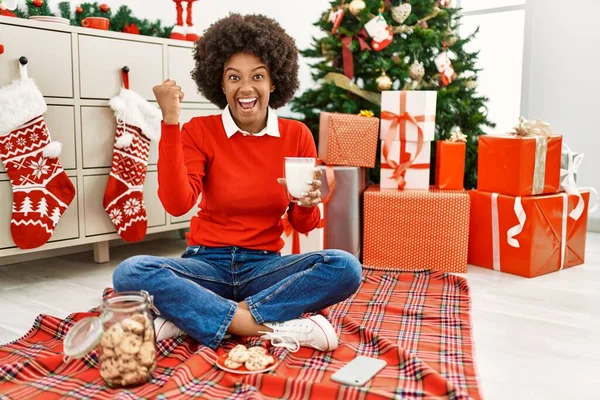 若いですアフリカ系アメリカ人女性とともにアフロの髪を食べるペストリー座っクリスマスツリーによって叫んで誇りに思って 勝利と成功を祝う非常に興奮して腕を上げ — ストック写真