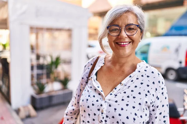 Orta yaşlı bir kadın sokakta kendine güvenerek gülümsüyor.