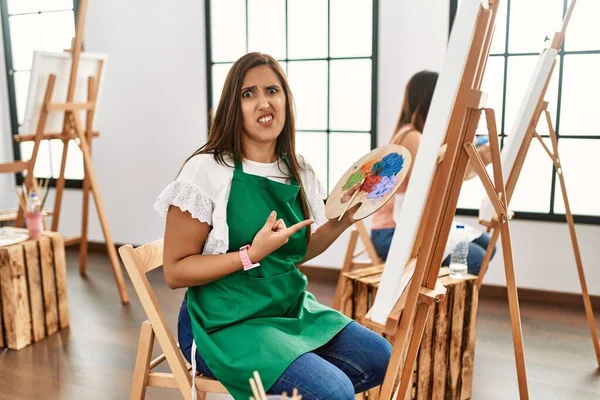 Young Hispanic Artist Women Painting Canvas Art Studio Pointing Aside — Stock Photo, Image