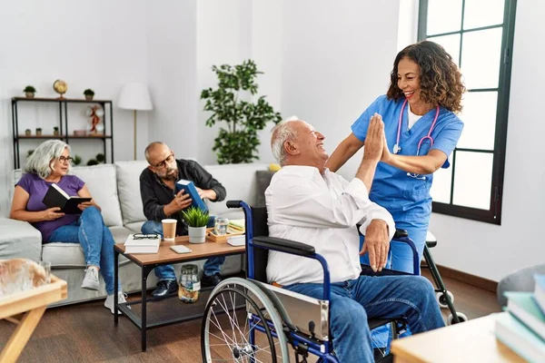 Middle age doctor woman and retired man sitting on wheelchair high five at nursing home.
