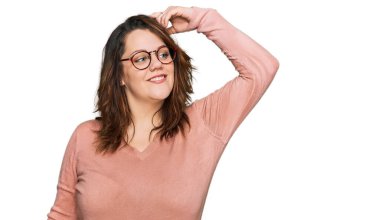 Genç ve cüsseli kadın günlük kıyafetler ve gözlük takıyor gülümsüyor saçlarına dokunuyor, el hareketi yapıyor, çekici ve modaya uygun poz veriyor. 