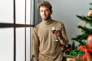 Genç İspanyol adam evde Noel ağacının yanında şarap içiyor.