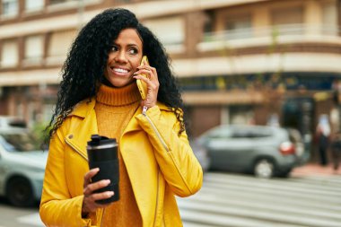Orta yaşlı Afro-Amerikalı kadın akıllı telefondan konuşuyor ve şehirde kahve içiyor..