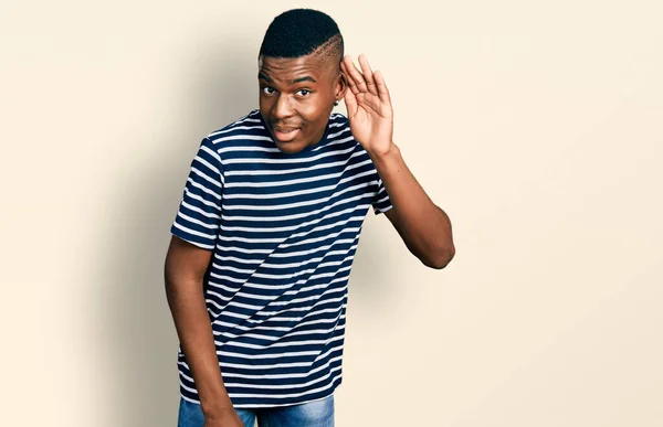 耳を傾け 噂やゴシップに耳を傾け手で笑みを浮かべてカジュアルな縞模様のTシャツを着て若いアフリカ系アメリカ人男性 聴覚障害の概念 — ストック写真