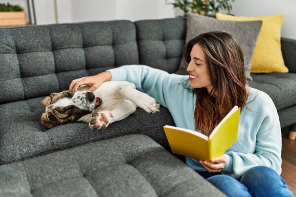Young woman reading book sitting with dog at home