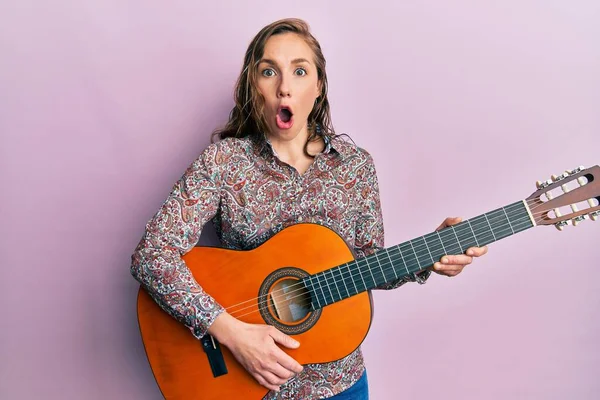 Jovem Loira Tocando Guitarra Clássica Com Medo Chocado Com Surpresa — Fotografia de Stock