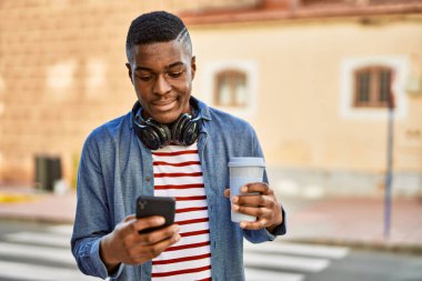 Genç Afrikalı Amerikalı adam akıllı telefon kullanıyor. Şehirde kahve içiyor..