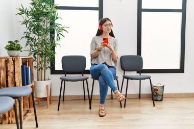 Bekleme odasında kulaklık takan genç Asyalı kadın.