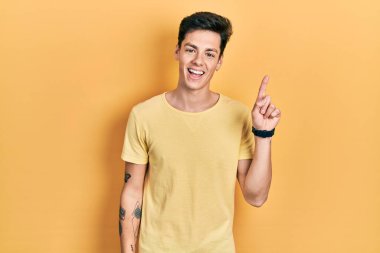 Gündelik sarı tişörtlü genç İspanyol adam başarılı bir fikri işaret ediyor. Heyecanlı ve mutlu. Bir numara.. 