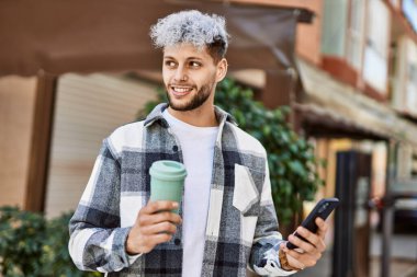 Genç İspanyol adam şehirde akıllı telefon kullanarak mutlu gülümsüyor..