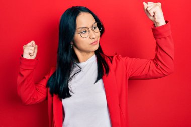 Güzel İspanyol kadın burun piercingli, sıradan görünüşlü ve gözlüklü gururla gülümseyen kol kaslarını gösteren. fitness konsepti. 