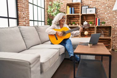 Orta yaşlı bir kadının evde online gitar dersi var.