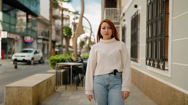 Sokakta ciddi bir ifadeyle duran genç kızıl saçlı kadın.