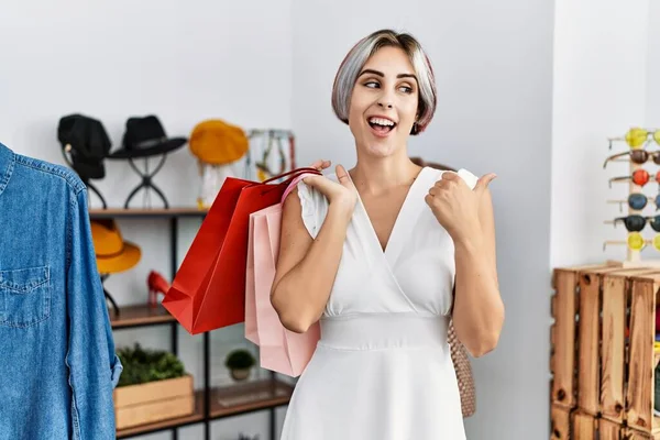 Alışveriş çantalarını mağazada elinde tutan genç ve güzel bir kadın baş parmağını kaldırarak gülümseyerek ağzı açık şekilde gülümsüyor. 