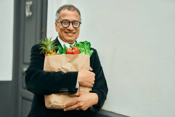 家のドアのそばに立っている新鮮な食料品の袋を持って笑っている中年東南アジアの男 — ストック写真