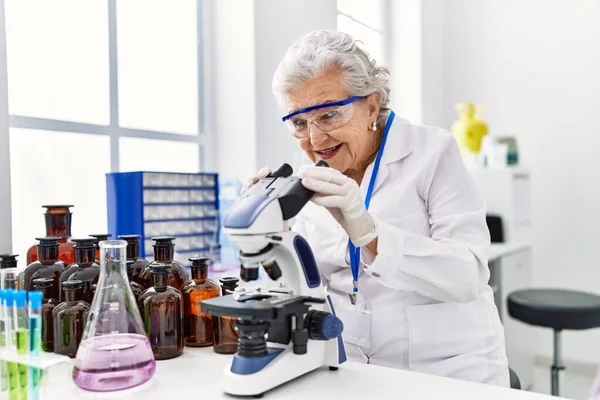 研究室で顕微鏡を使って科学者の制服を着たシニア白髪の女性 — ストック写真