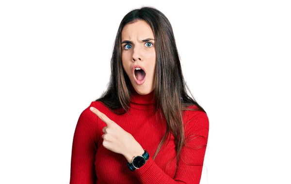 Young Brunette Teenager Wearing Red Turtleneck Sweater Surprised Pointing Finger — стоковое фото