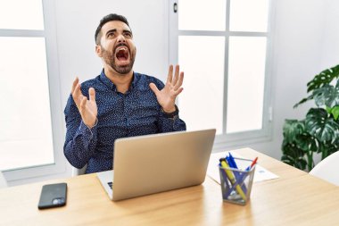 Ofiste sakallı, deli deli dizüstü bilgisayarla çalışan sinirli, agresif bir ifade ve kollarla bağıran genç bir İspanyol. hüsran kavramı. 