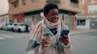 Genç Afrikalı Amerikalı kadın akıllı telefon kullanıyor. Sokakta kahve içiyor.